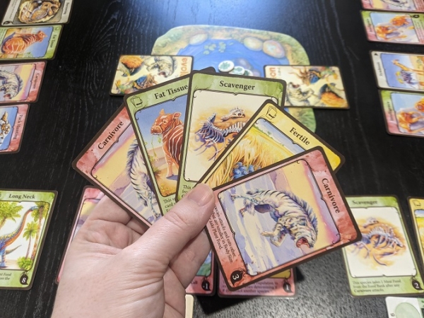 What it looks like in game of Evolution, I have a hand of cards, there's a watering hole in the middle with creatures either side.